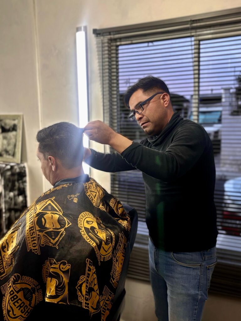 Hombre cortando terminando de cortar el cabello y peinando a un cliente en la Barbería Green en Pachuca.